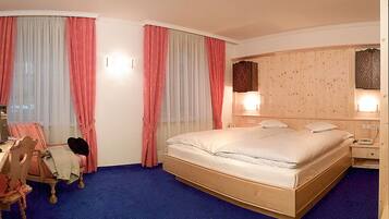 Quarto de hotel com cama de madeira, uma escrivaninha com cadeira e mesa de cabeceira com abajur.