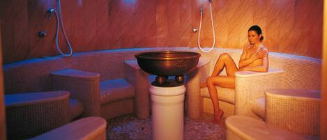 Un vestíbulo de sauna con una gran cuenca central, varios rincones de descanso e iluminación en el techo.