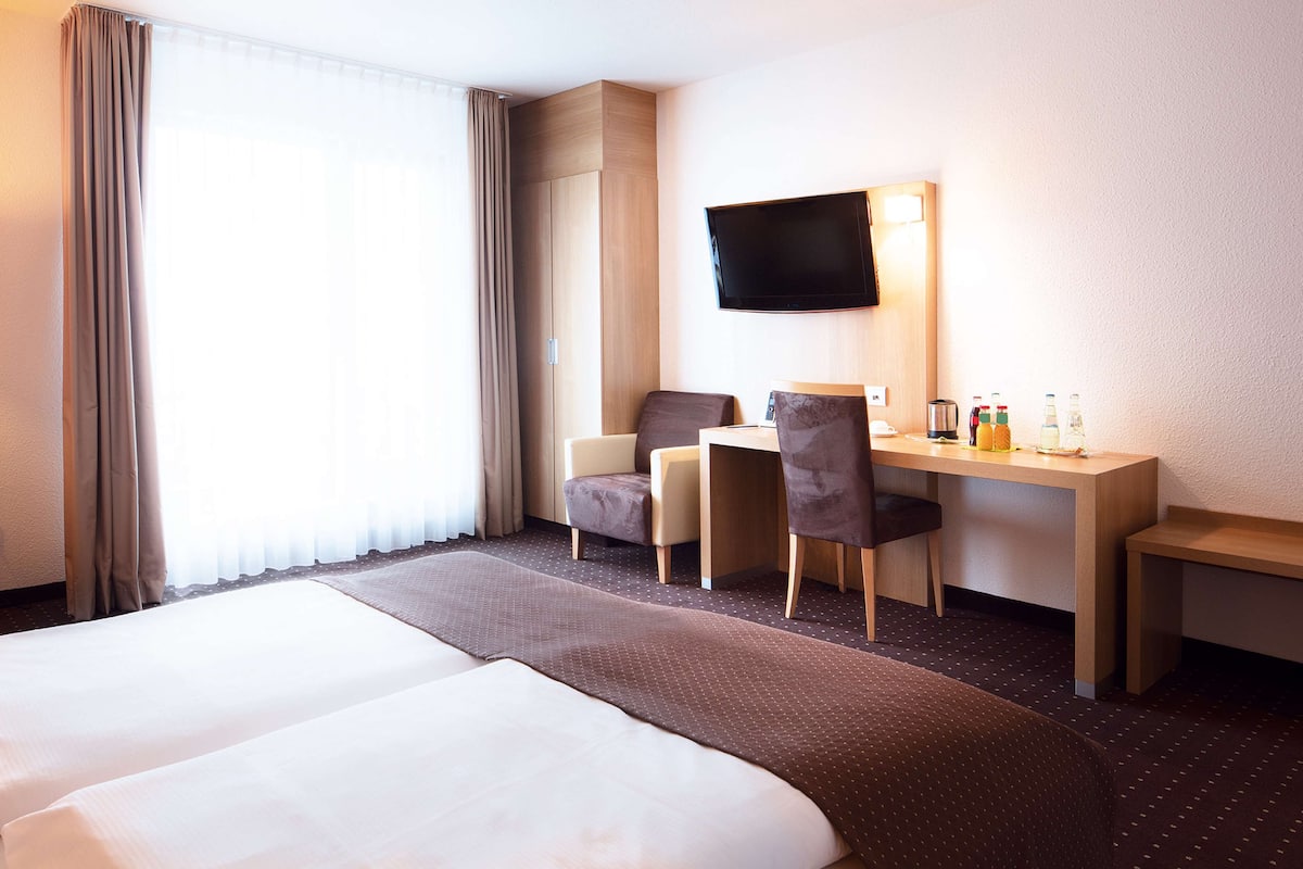 Habitación de hotel con una cama grande, un escritorio con dos sillas, un televisor de pantalla plana y un minibar.