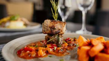 A plated dish with a meat centerpiece, garnished with rosemary, accompanied by a side of diced vegetables and a sauce.