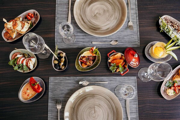 Mesa de comedor lista con platos, vasos y diversos platillos, indicando una preparación para la comida.