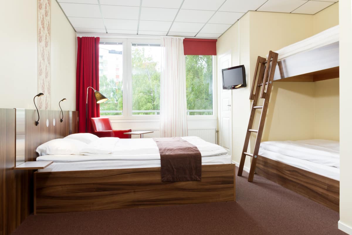 Une pièce avec un lit en bois, une chaise rouge, un bureau, un téléviseur et une fenêtre avec des rideaux.