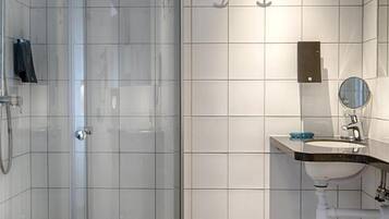 Ett modernt badrum med en dusch som är avskärmad med glasväggar, ett vitt handfat med en spegel och en toalett.