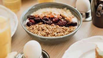 En frukostuppläggning med en skål müsli, en kopp kaffe och olika frukter och bakverk på ett träbord.