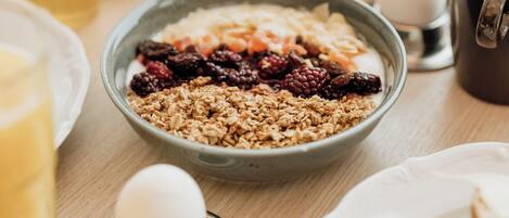 Colazione con una ciotola di granola, una tazza di caffè e diversi tipi di frutta e dolci su un tavolo di legno.