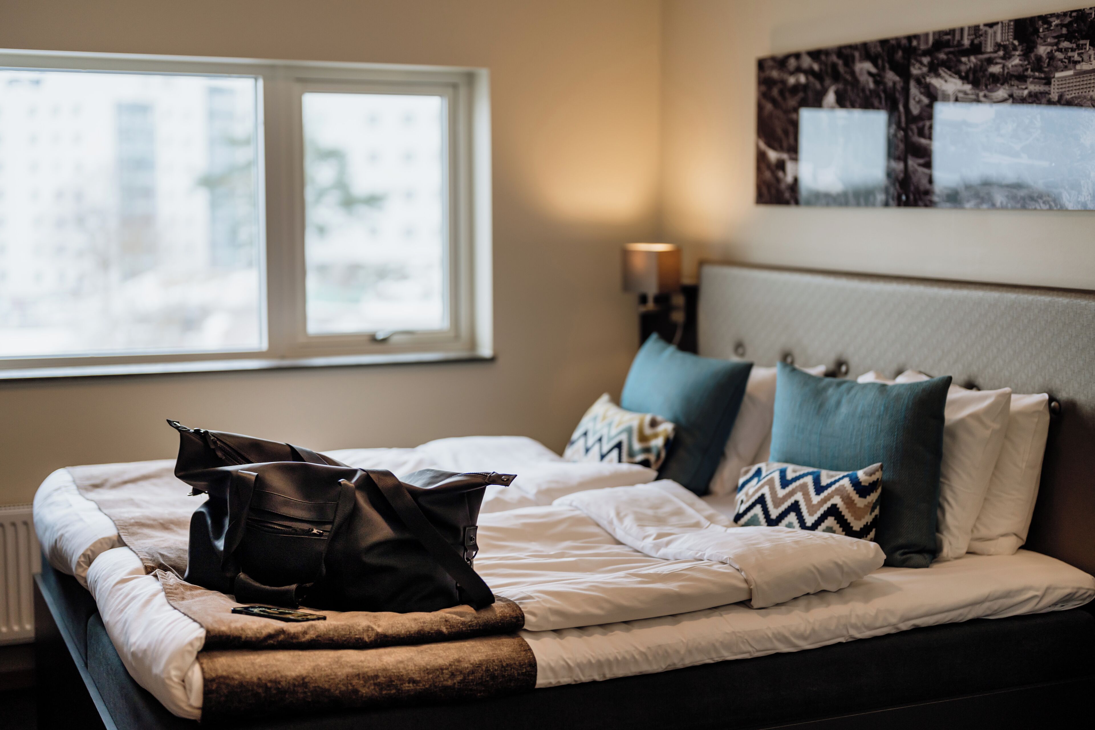 A neatly made bed with a black bag, pillows, and a blanket.