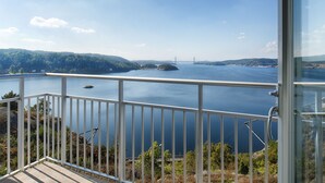 Un balcon offrant une vue sur une vaste étendue d’eau, un pont et un paysage boisé.