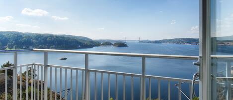 A balcony with a view of a large body of water, a bridge, and a forested landscape.