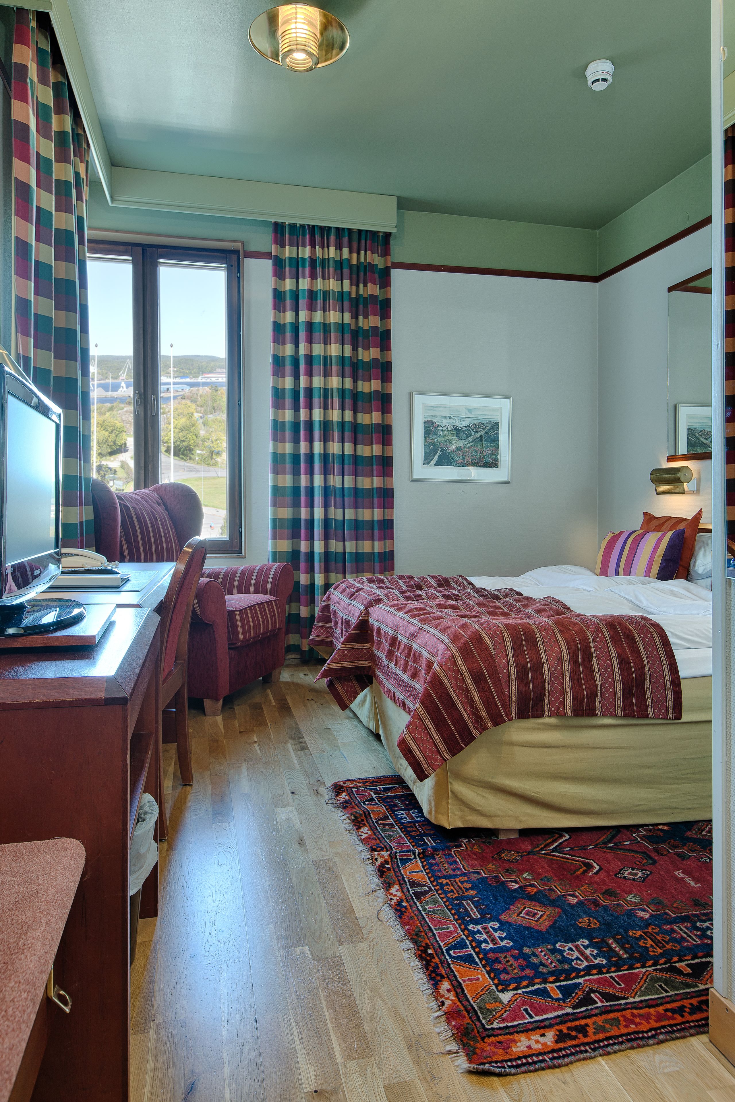 Un dormitorio con escritorio, silla, cama y vistas al exterior a través de una ventana.