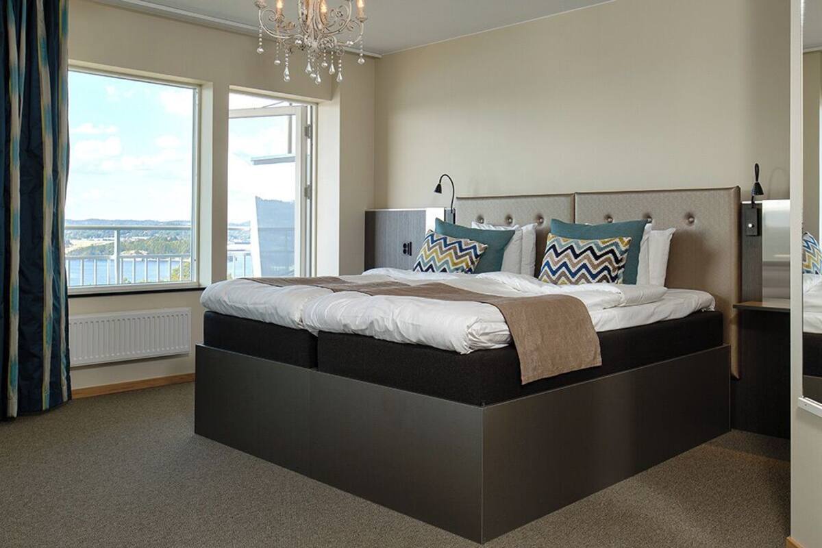 Une chambre moderne avec un grand lit, une vue sur l’extérieur et un lustre.