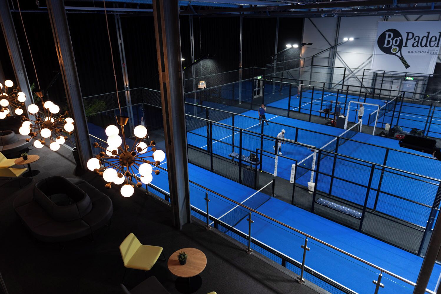A multi-level indoor sports facility with blue flooring, a netted tennis court, and a billiards area.