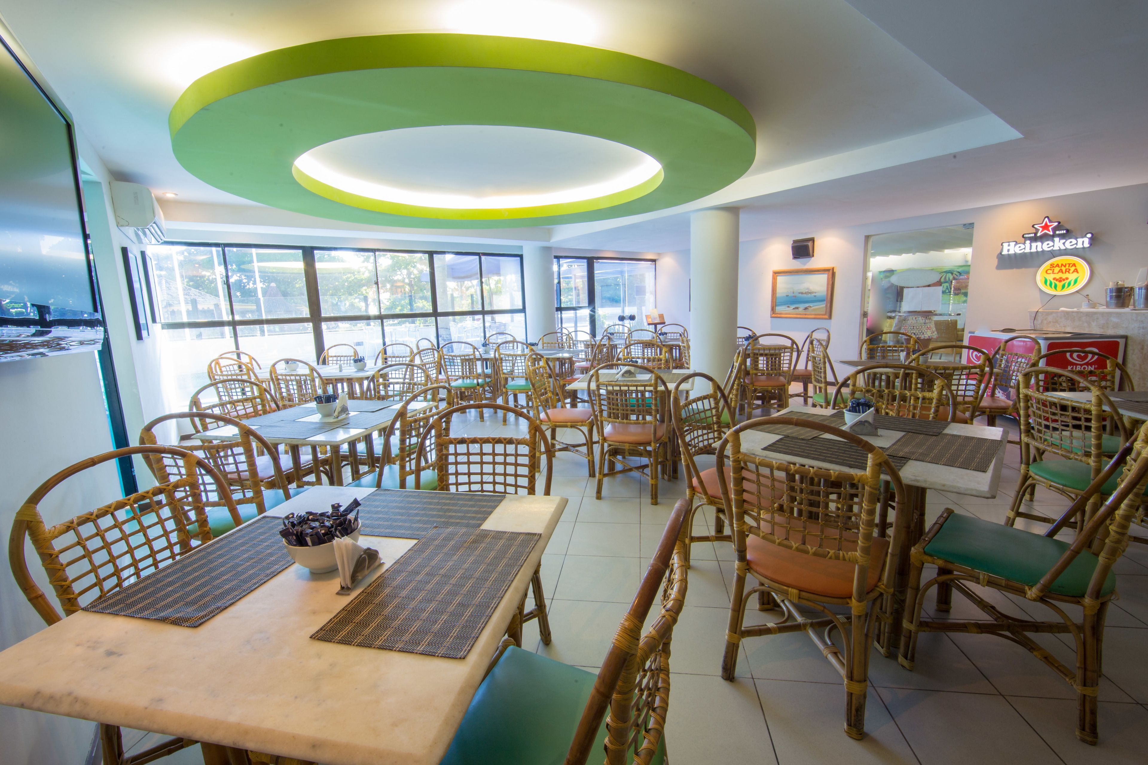 A restaurant interior with wicker furniture, large windows, and a Heineken sign.
