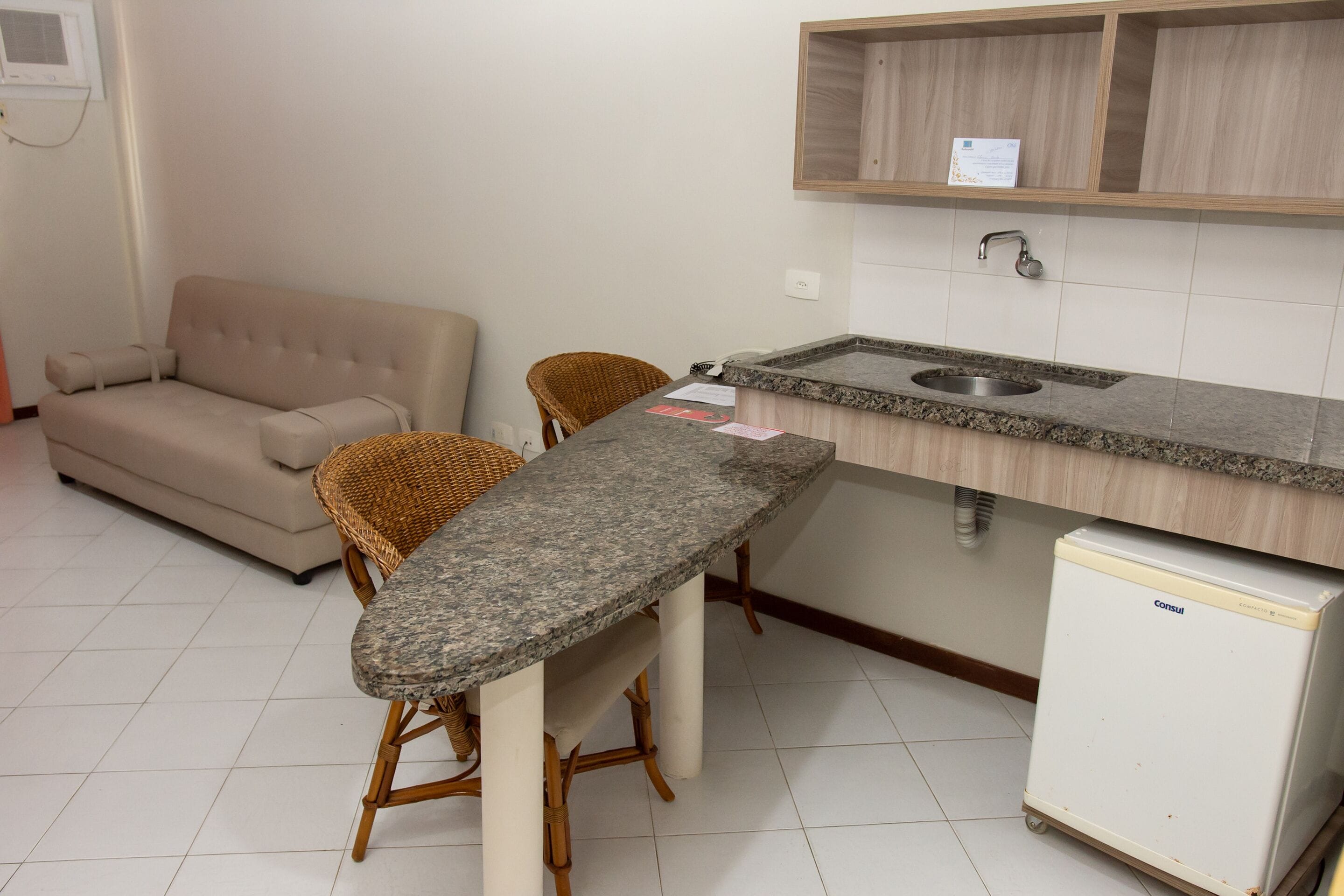 A compact kitchen with a granite countertop, a small refrigerator, a built-in sink, and a beige sofa.