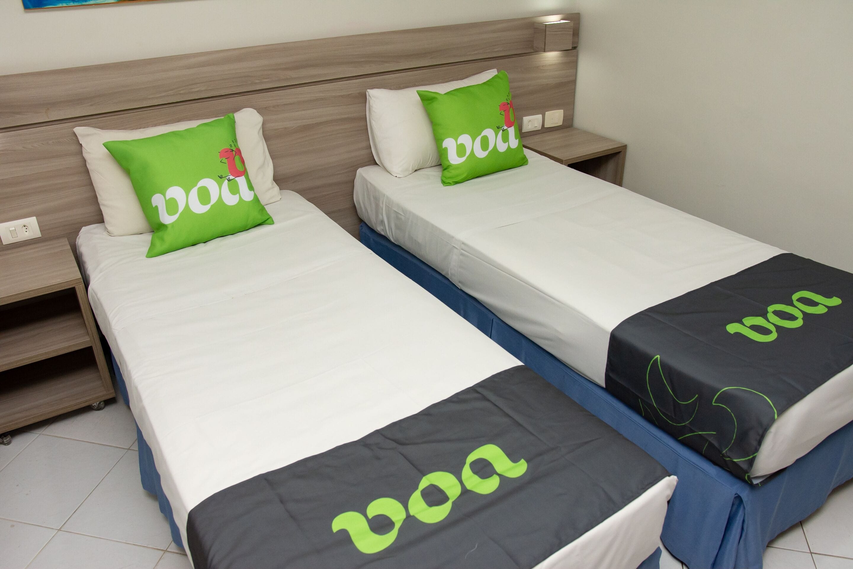 Two twin beds with white and black bedding, each with a green pillow featuring the word "boa".