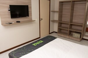 A bedroom with a bed, a TV mounted on the wall, a wardrobe, and a small shelf with remote controls.