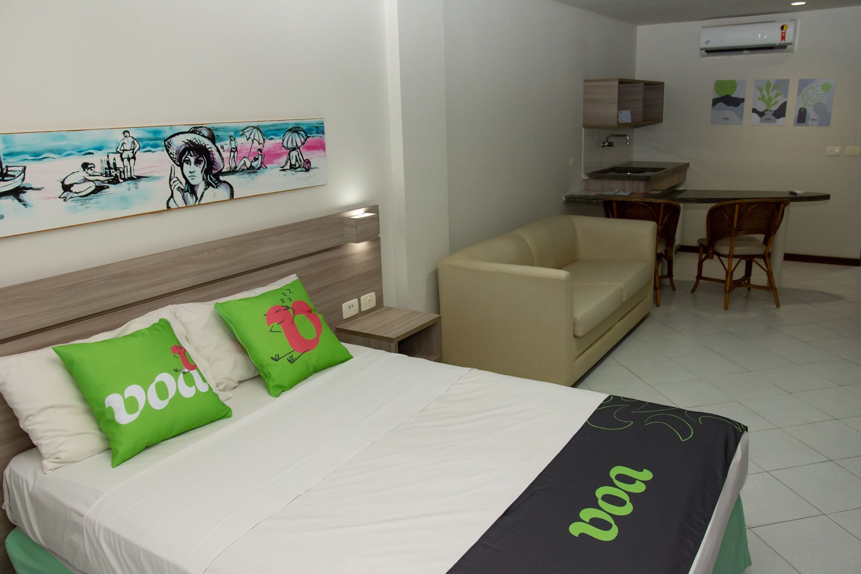 A hotel room with a bed, a sofa, a dining table, and a kitchen area.