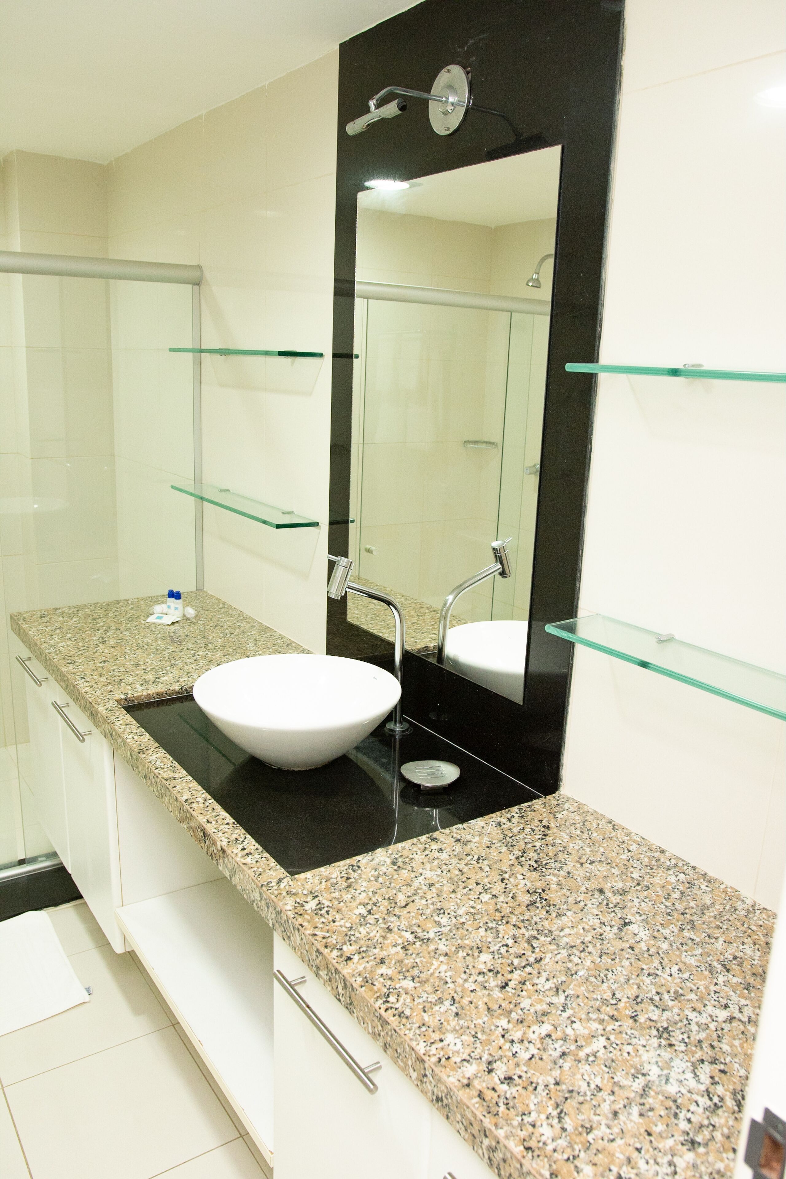 A bathroom with a granite countertop, a white sink, a glass shelf, and a mirror.