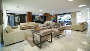 A spacious lobby with multiple seating areas, a reception desk, and a visible elevator. - Like U Hotel Brasilia (Brasília)