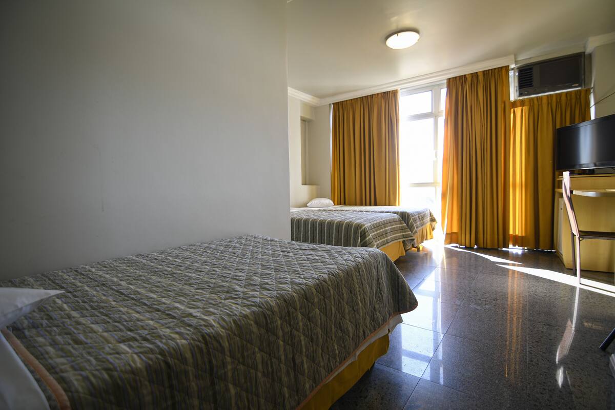 Quarto de hotel com duas camas, televisão de tela plana e janela com cortinas.