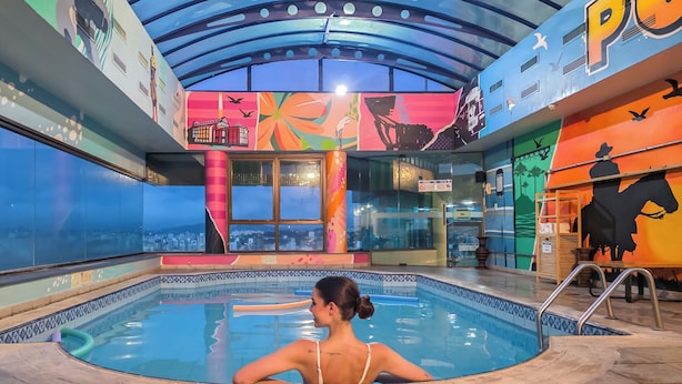 Una piscina con vistas a un paisaje urbano, un mural colorido y un cartel que indica zona para no fumadores.
