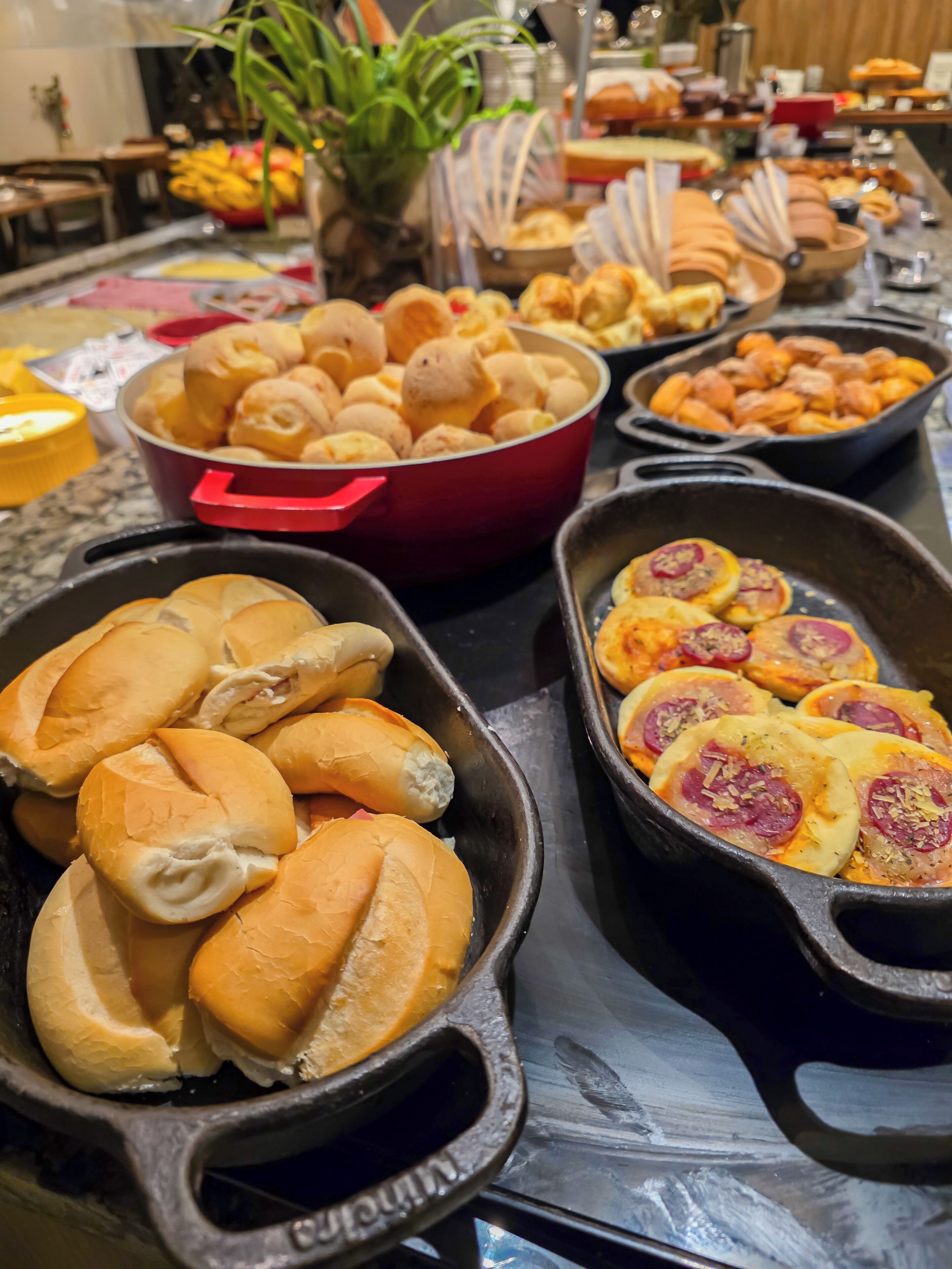 A buffet table with various food items including rolls, pastries, and a cast iron skillet with sliced meats.
