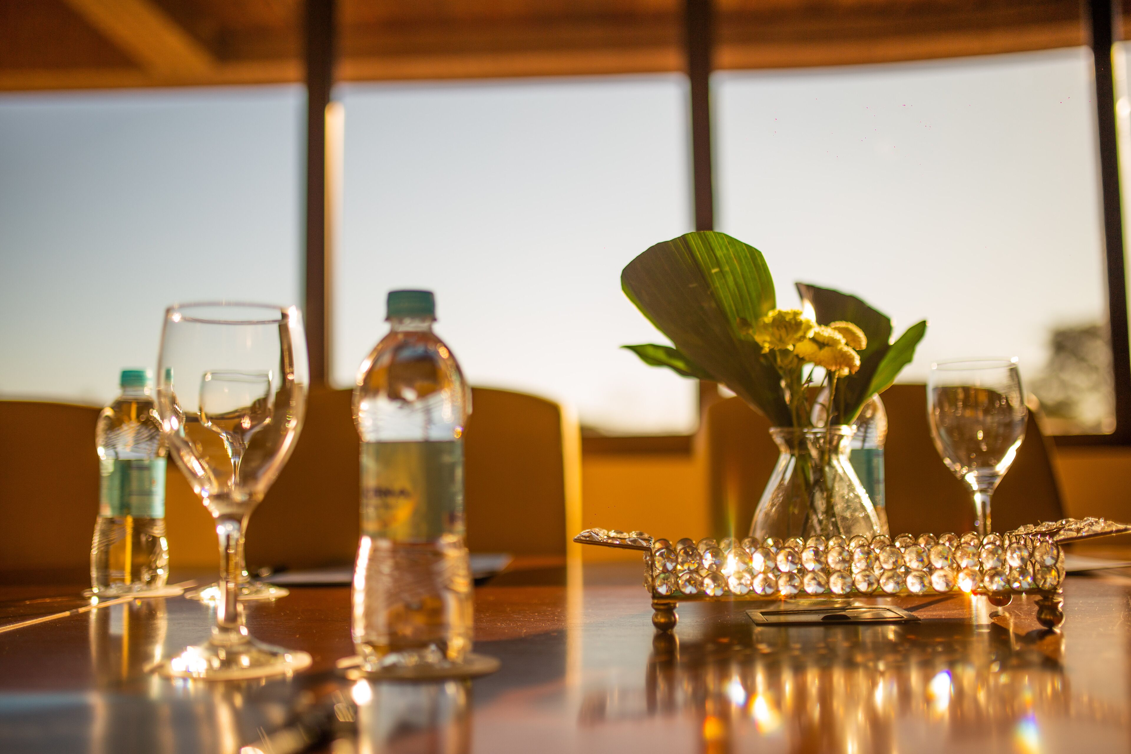 Een tafel met een glazen vaas met gele bloemen, een glazen decanter en een wijnglas.