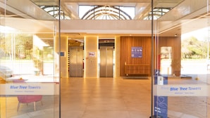 La entrada de Blue Tree Towers con fachada de vidrio, ascensores y un mostrador de recepción de madera.