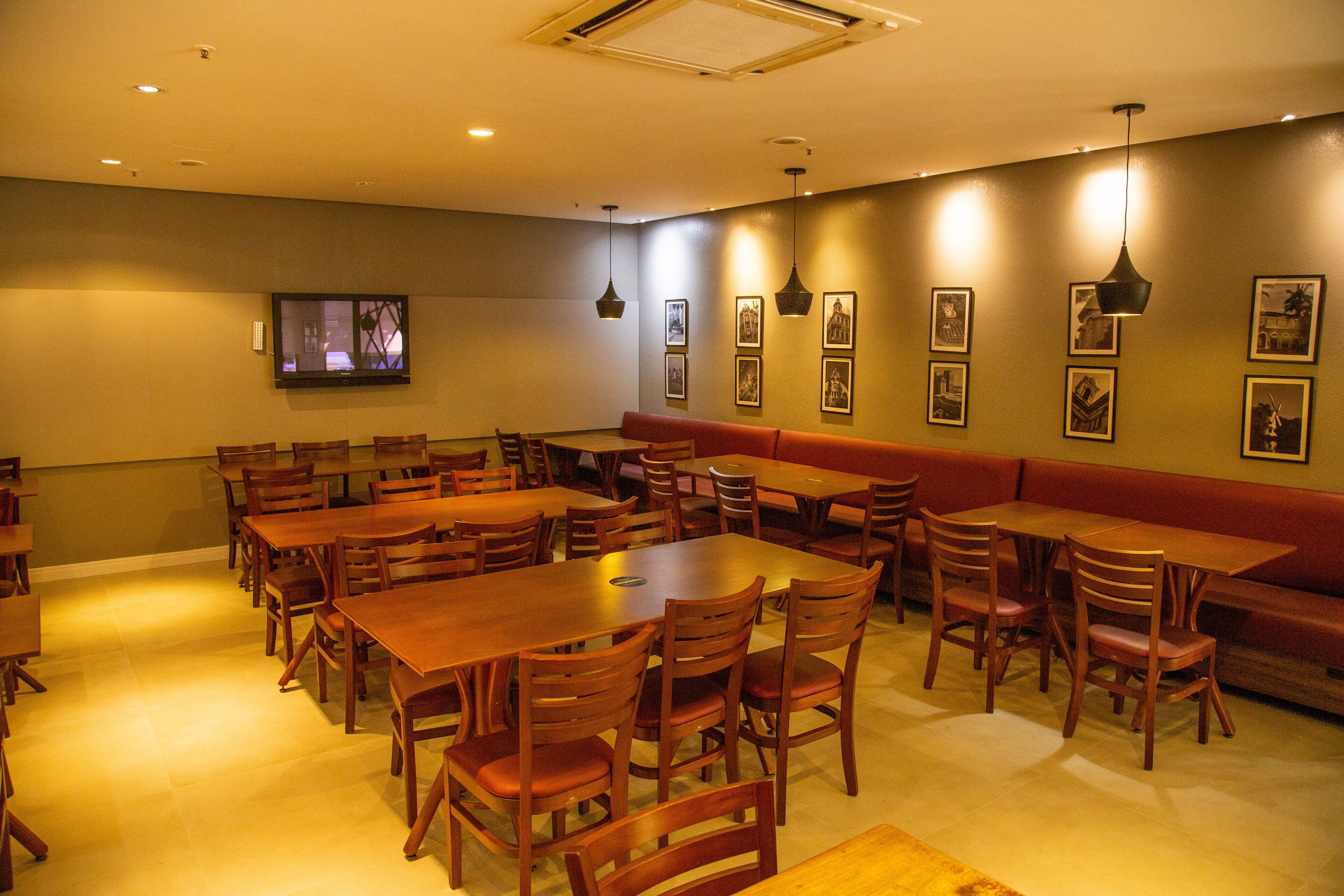 A restaurant with multiple wooden tables and chairs, a television mounted on the wall, and framed pictures on the wall.