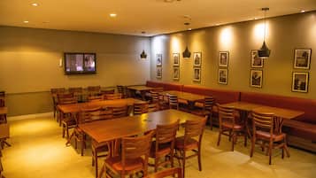 A restaurant with multiple wooden tables and chairs, a television mounted on the wall, and framed pictures on the wall.