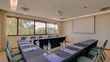 A conference room with a long table, chairs, water bottles, and a projector screen.