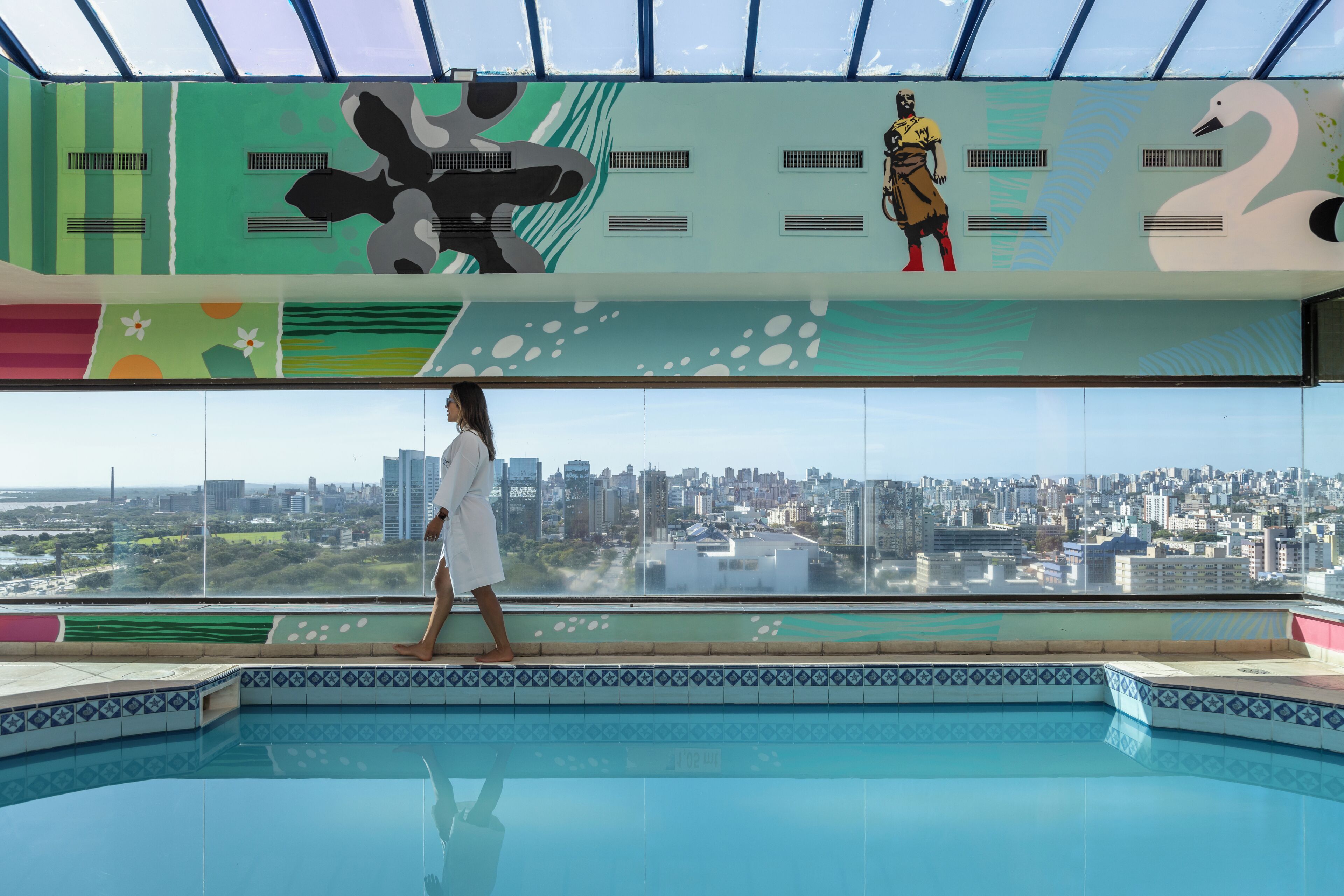 A pool area with a city view, a person walking, and a mural with abstract designs.