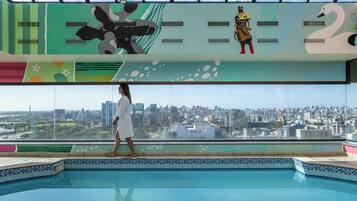 A pool area with a city view, a person walking, and a mural with abstract designs.
