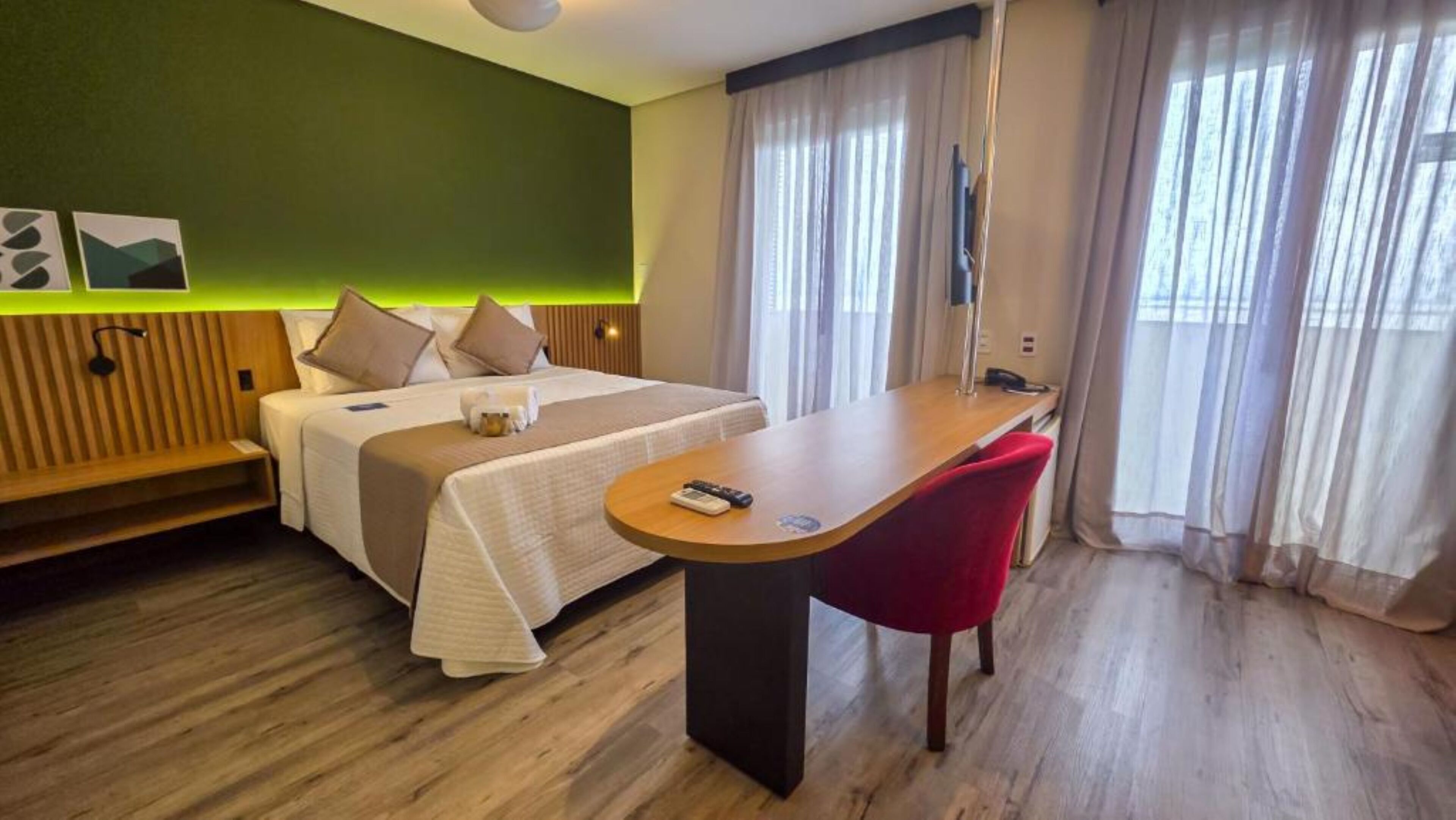 Una habitación de hotel con una cama, un escritorio, una silla roja y un banco de madera.