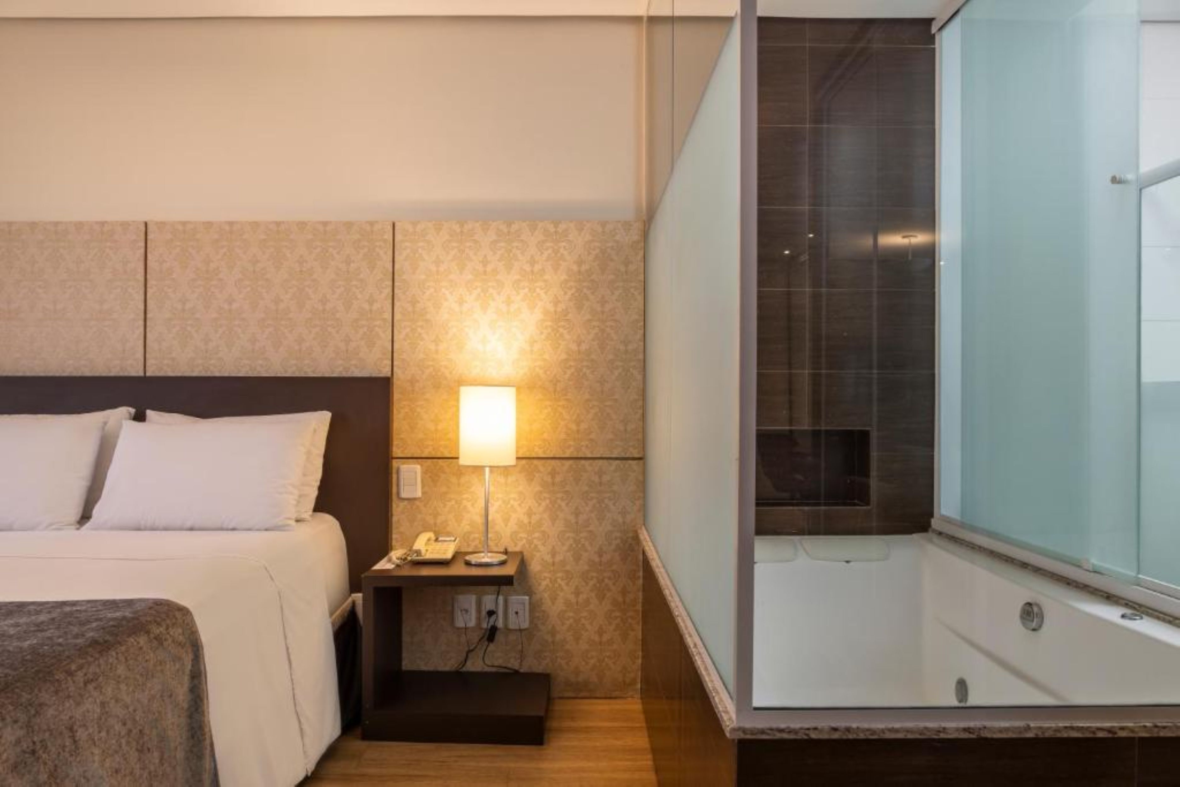Una camera d'albergo con un letto, un comodino con una lampada e un angolo doccia.