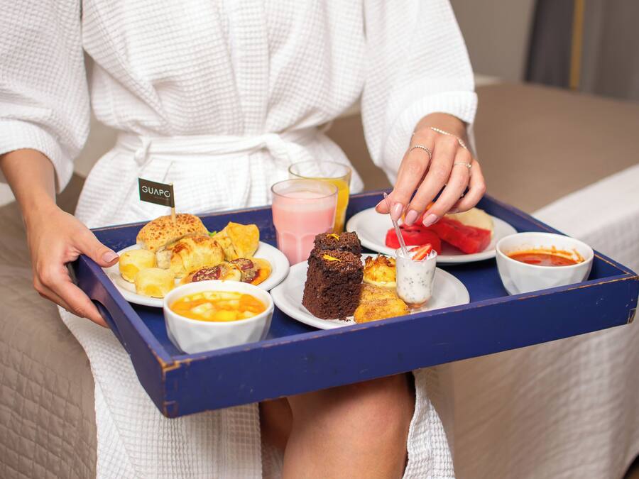 A person holding a tray with various food items and a drink.
