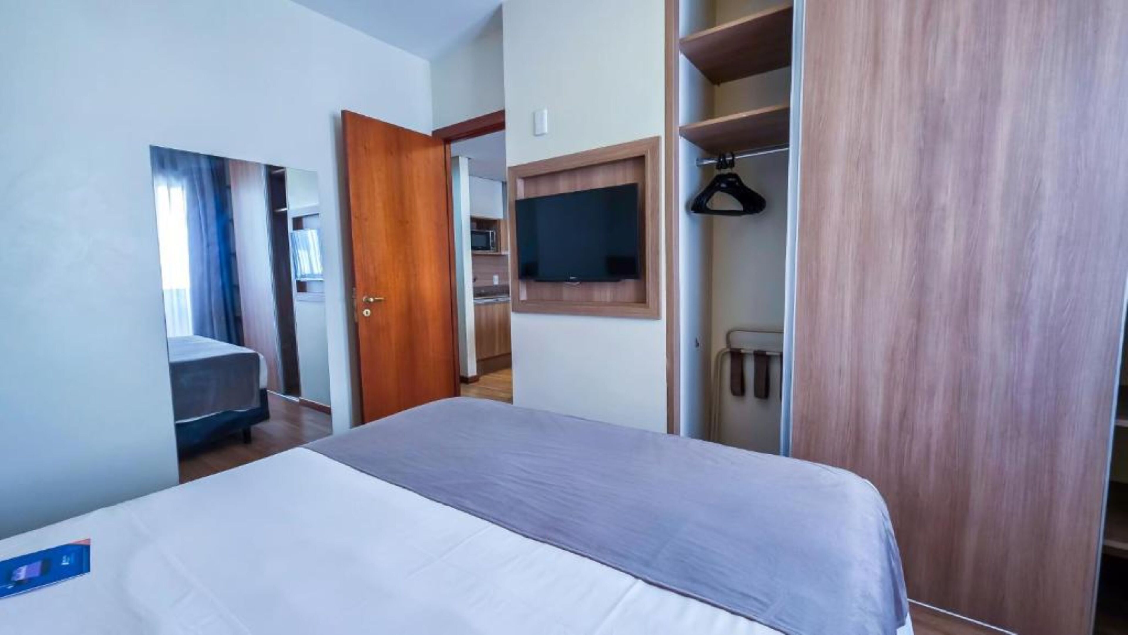 Habitación de hotel con cama, televisor montado en la pared, armario y baño visible a través de una puerta abierta.