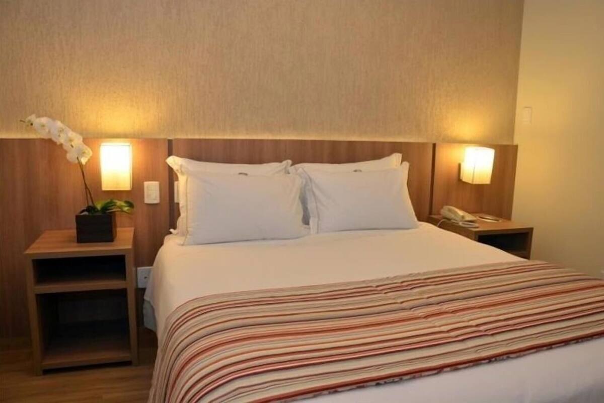 Ein Hotelzimmer mit einem Bett, zwei Nachttischen, einer Topfpflanze und Wandlampen.