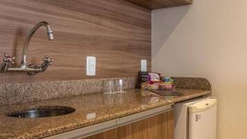 A kitchen with a granite countertop, a stainless steel sink, a microwave, and wooden cabinetry.