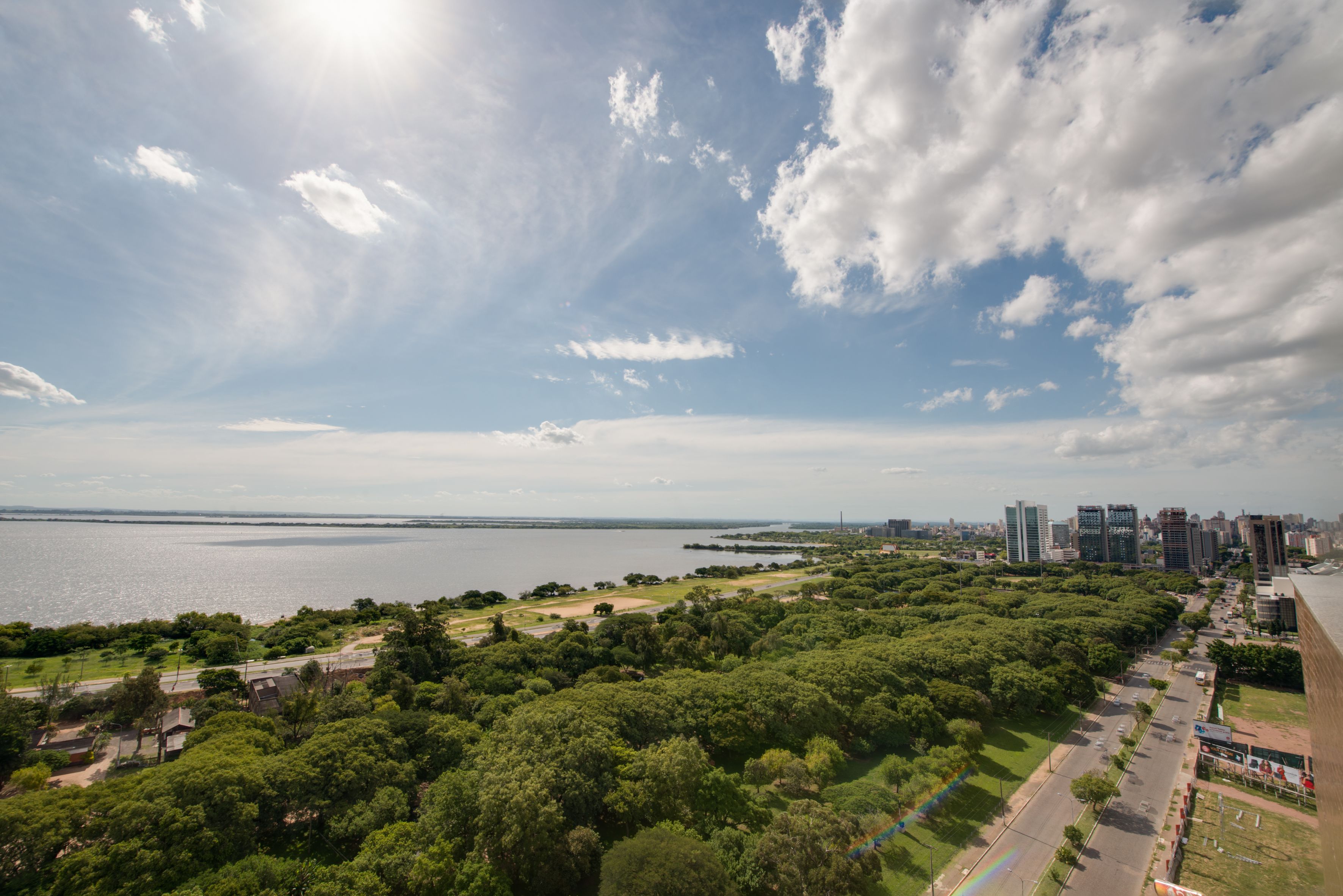 Vista panorámica de un parque con un río, una carretera y el perfil de una ciudad al fondo.
