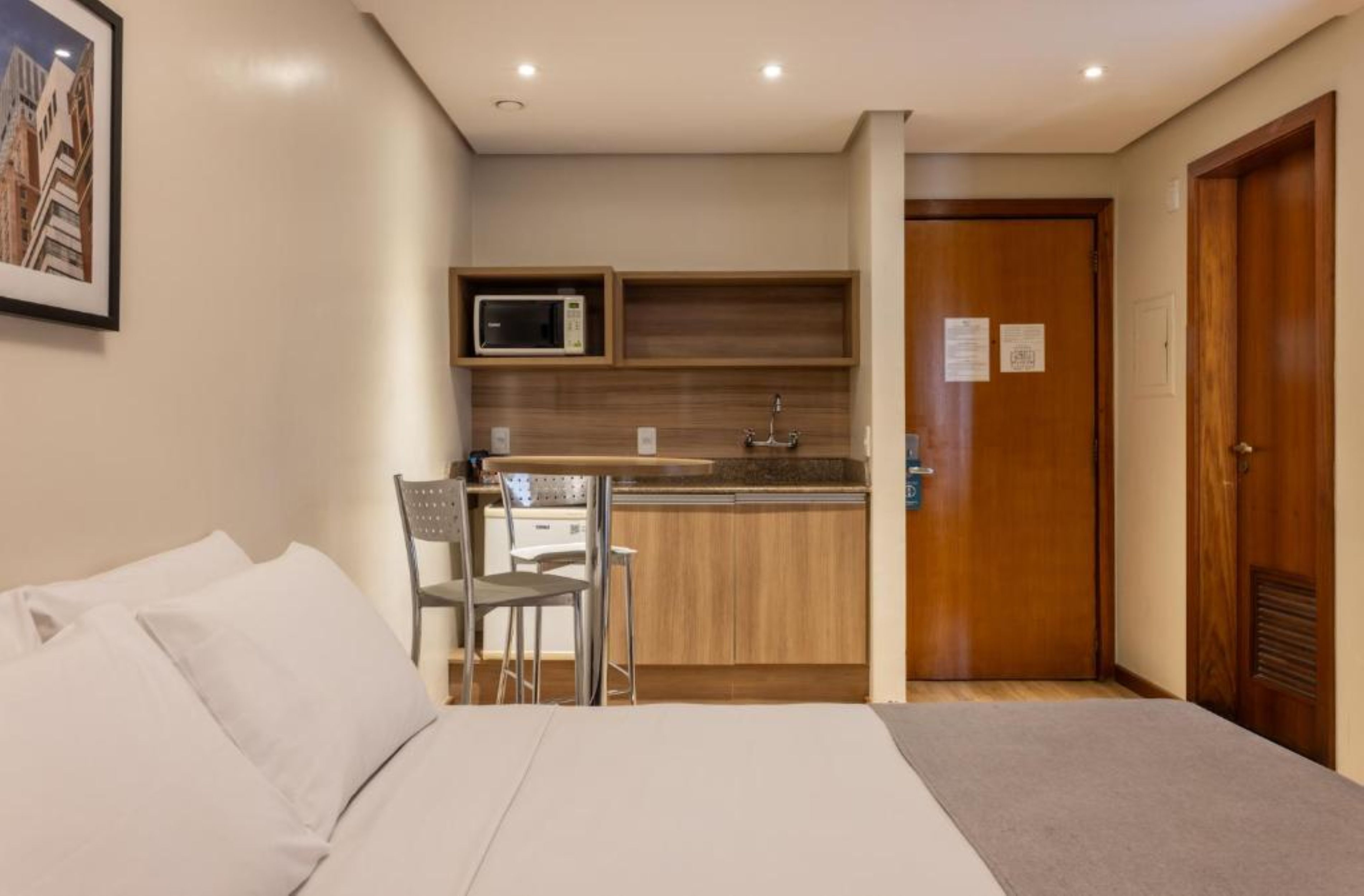 A hotel room with a bed, a small kitchenette, a dining area, and a door.