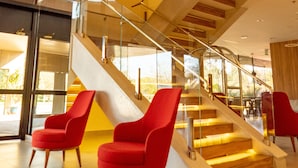 Un interior moderno con una escalera, sillas rojas y grandes ventanales.