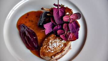 A plate with a piece of meat, a dark vegetable, and purple leaves.