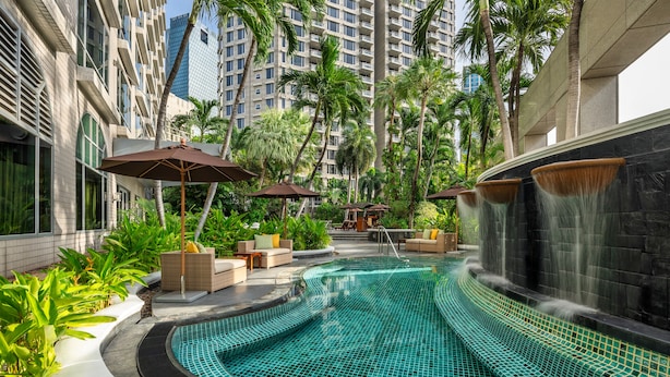 Piscina con caída de agua, rodeada de palmeras y mobiliario exterior.