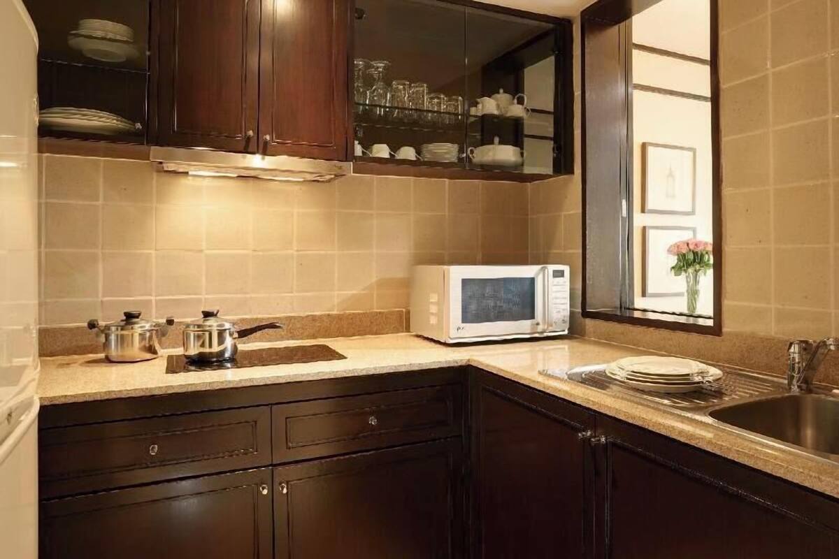 Una cocina con armarios de madera oscura, un microondas blanco y una ventana con un florero.