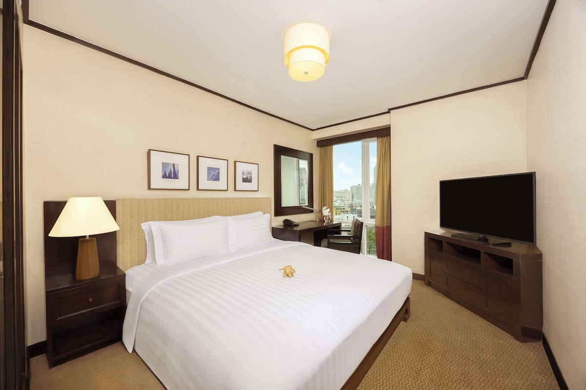Habitación de hotel con una cama grande, un televisor de pantalla plana, un escritorio con lámpara y una ventana con vista a la ciudad.