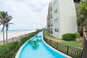 A swimming pool with water slides, a beach, and a multi-story building with balconies. - Beach Park Acqua Resort (Aquiraz)