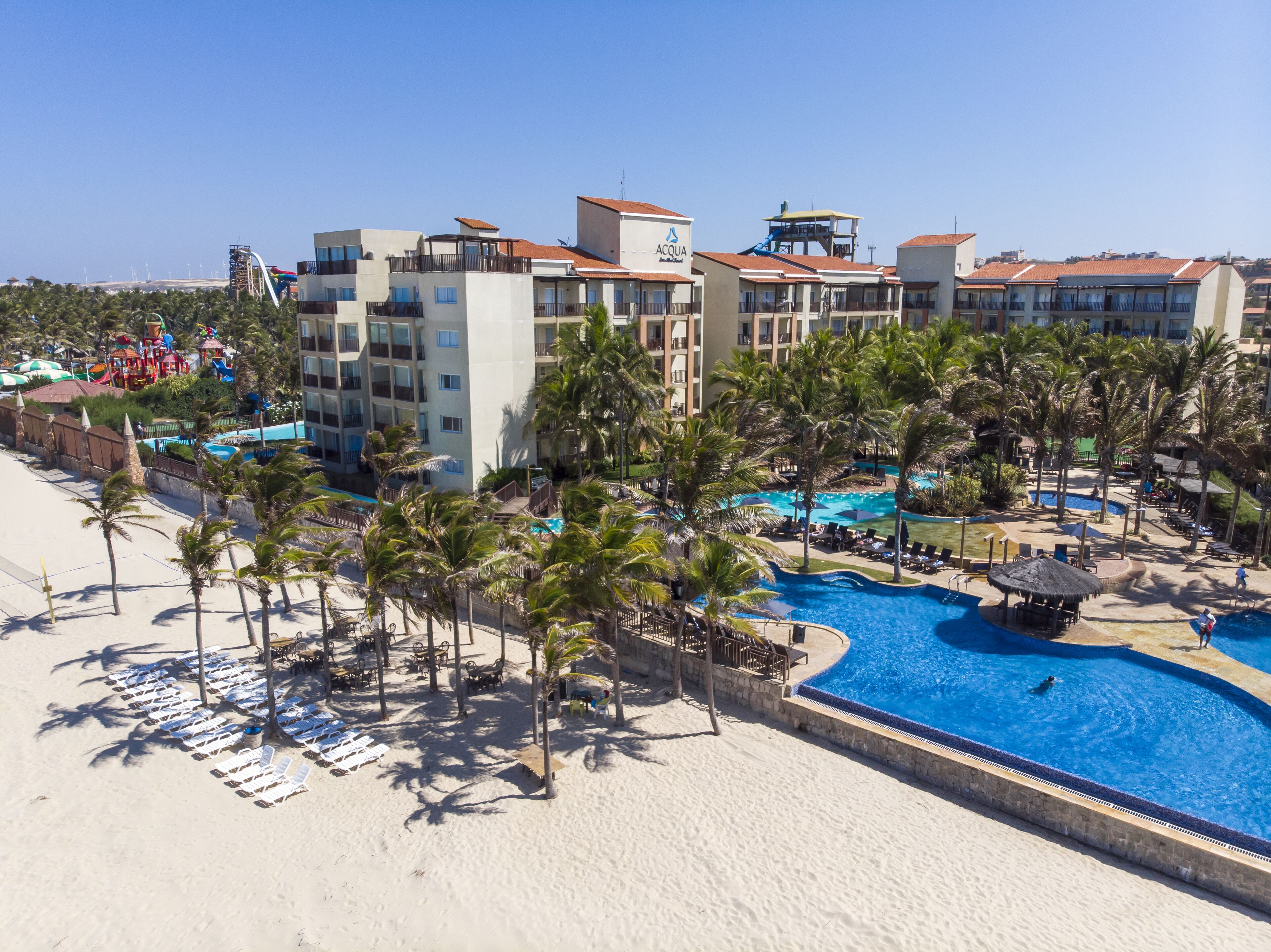 A resort with a swimming pool, palm trees, and beach chairs.