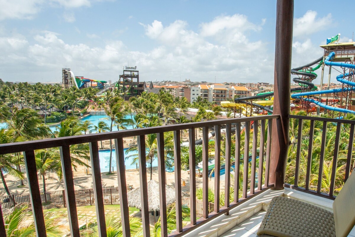 Un balcón con vistas a un parque acuático, que incluye una piscina de olas y una piscina.
