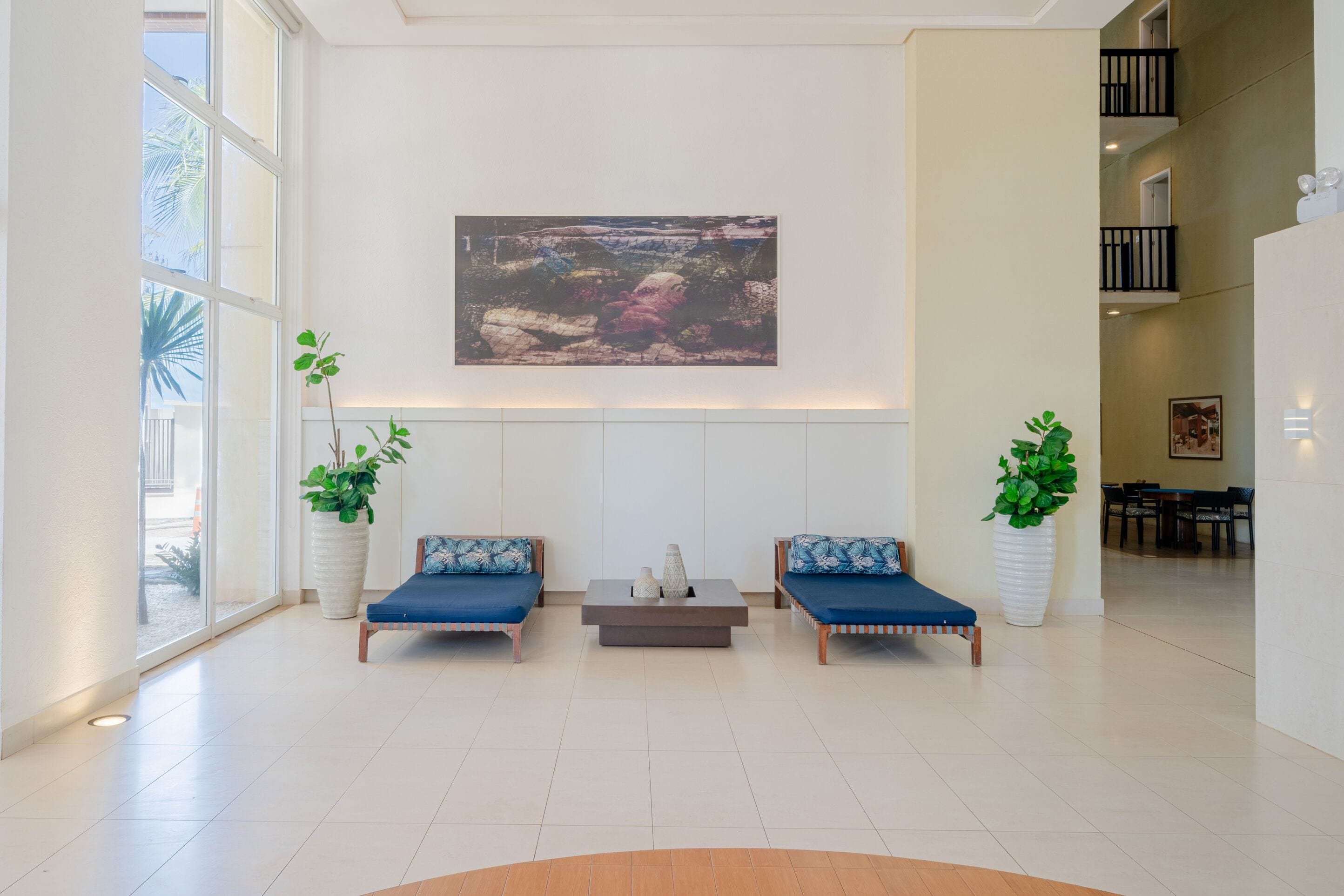 A spacious lobby with two blue sofas, a coffee table, and large potted plants.