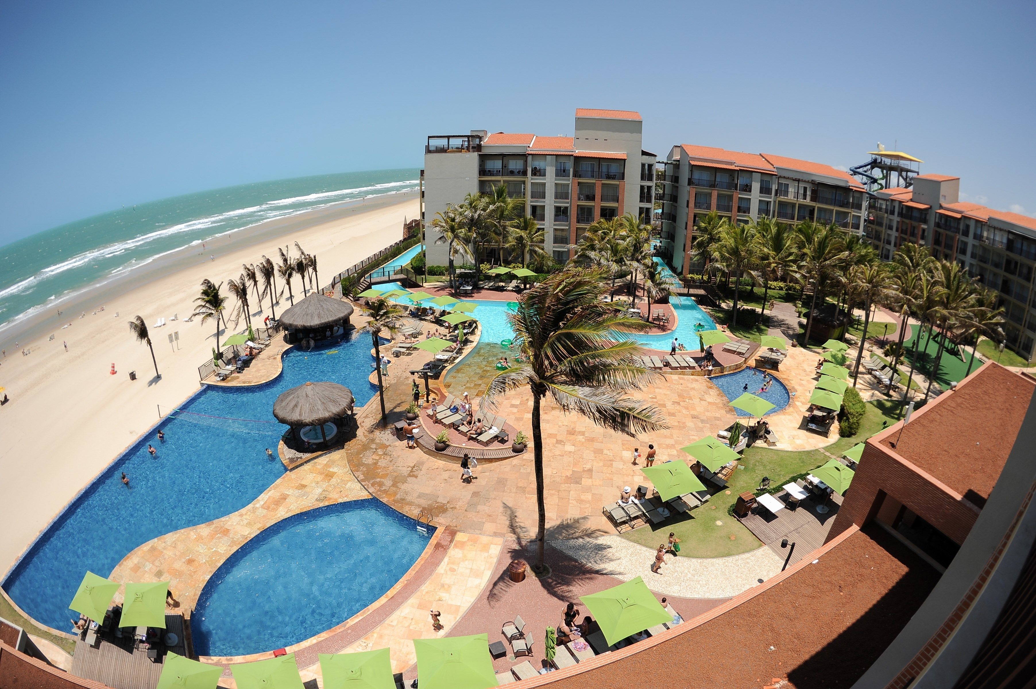 A resort with a large pool area, a beach, and a building with multiple balconies overlooking the ocean.